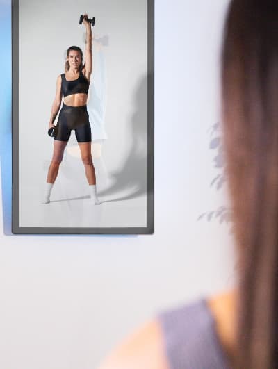 roflect-tv-mirror-07 Woman standing in front of a vertical Roflect mirror TV screen working out along with the woman on screen holding up a dumbell.